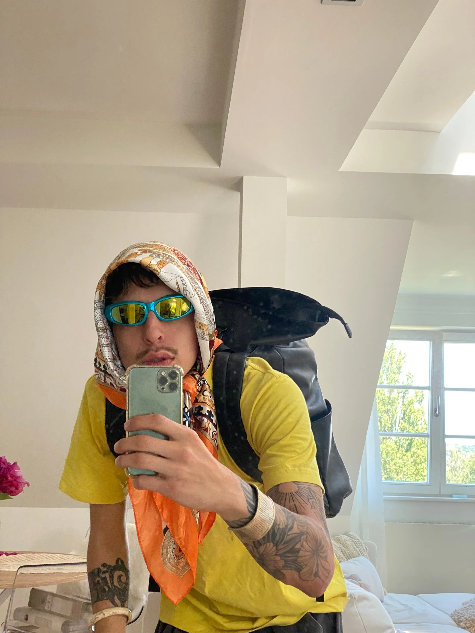 Markus “MJ” Langrock taking a mirror selfie in a patterned headscarf, blue sunglasses and a yellow shirt